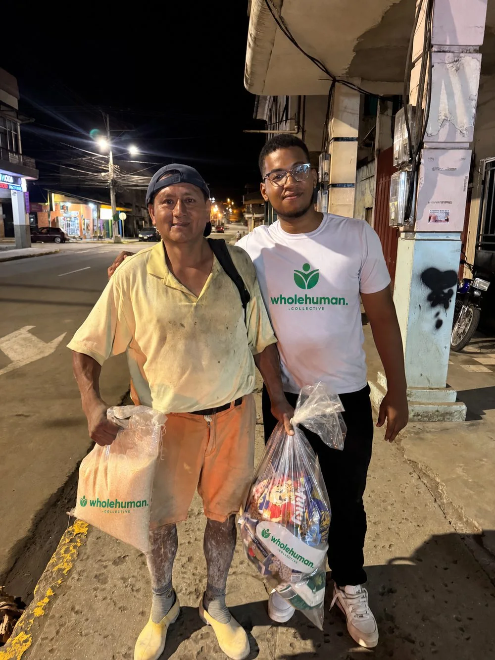 A man holding groceries beside a Wholehuman team member on a street at night